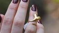 Hand wearing a gold ring with a blurred natural background