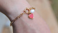 Gold bracelet with heart charm on a wrist against a blurred background