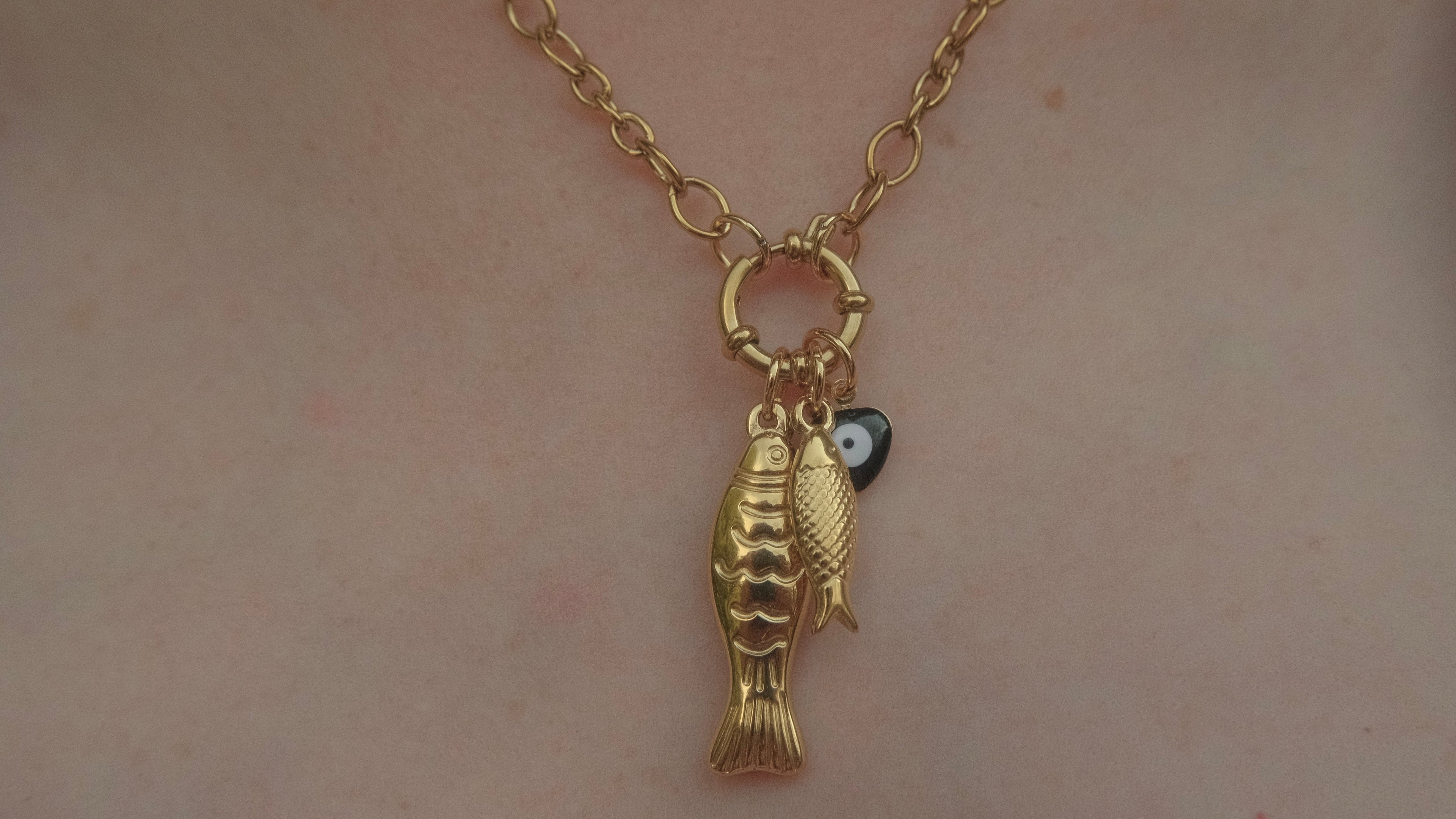 Gold fish-shaped pendant on a chain against a neutral background
