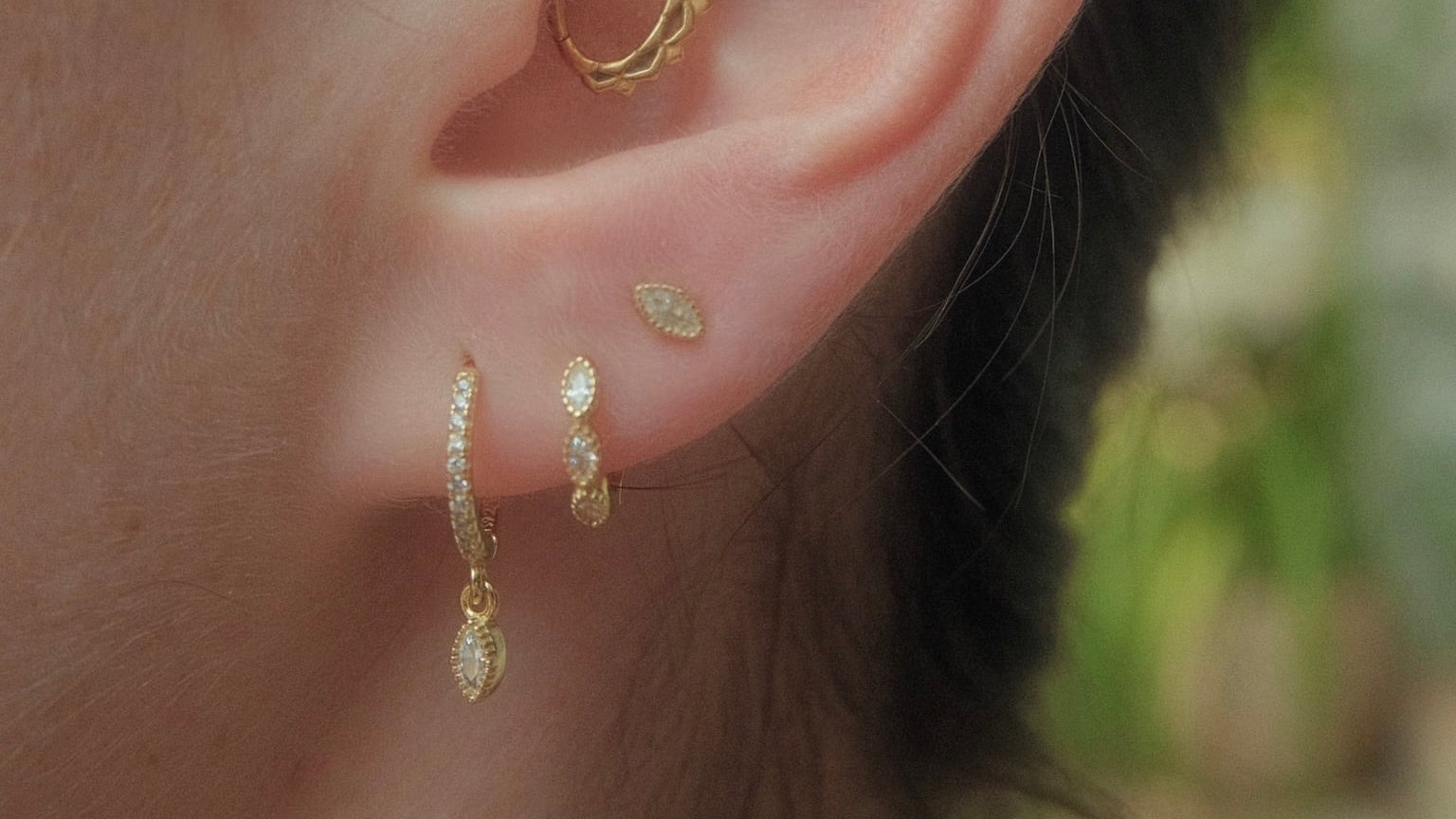 Close-up of an ear wearing gold hoop and stud earrings with a blurred background