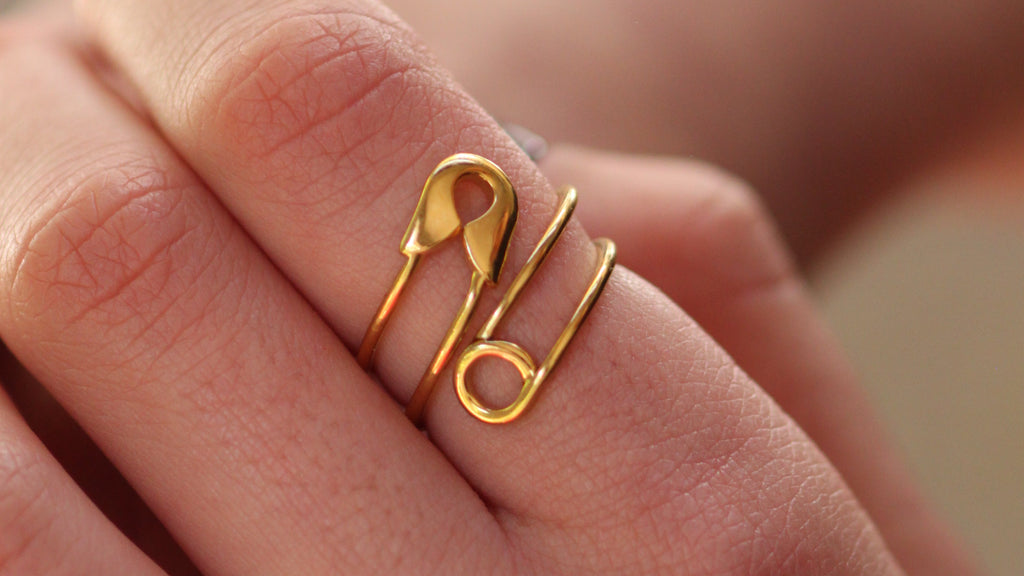 A close-up of a person's hand wearing a delicate gold safety-pin style ring.