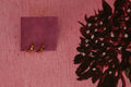 Two small gold rings displayed on a small purple square card against a pink textured background with a dark floral print in the top corner.
