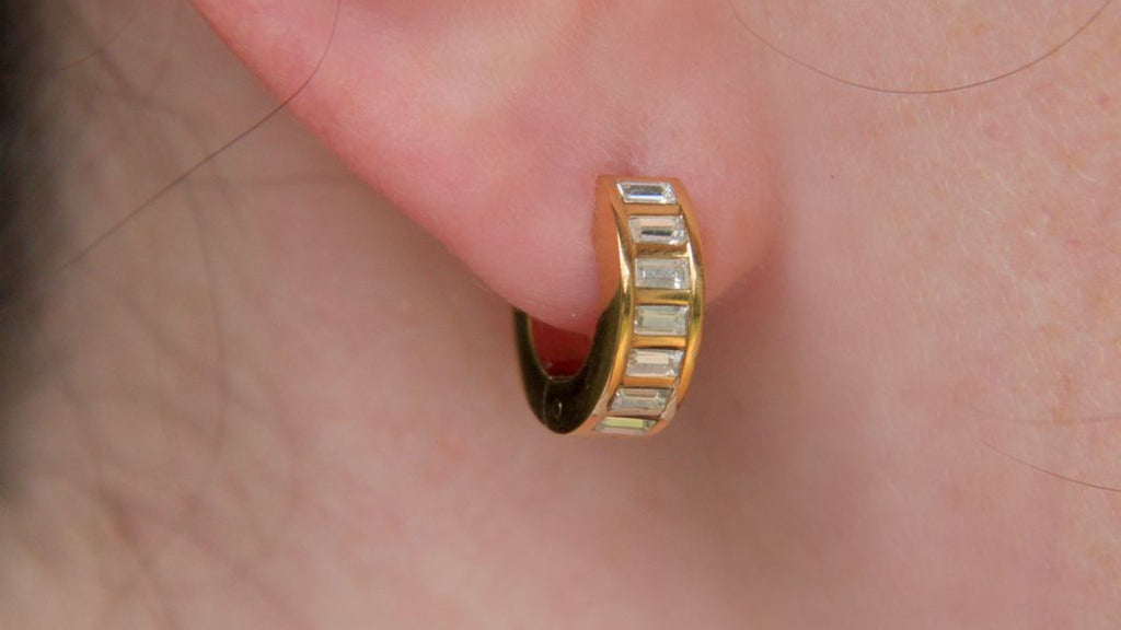 Gold hoop earring with embedded stones worn on an ear