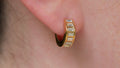 Gold hoop earring with embedded stones worn on an ear