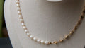 Pearl necklace on a mannequin bust with 'Silvi Mick' label against a blurred green background