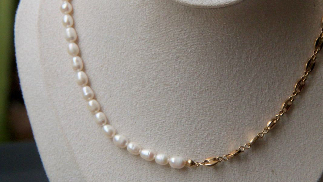 Pearl necklace on a mannequin bust with 'Silvi Mick' label against a blurred green background