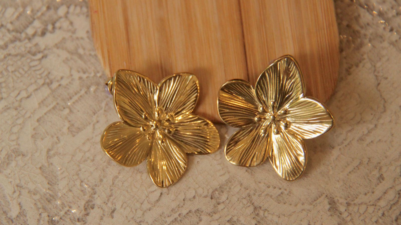 Gold floral earrings on a textured surface