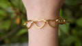 Gold heart-shaped bracelet on a wrist with a blurred green background