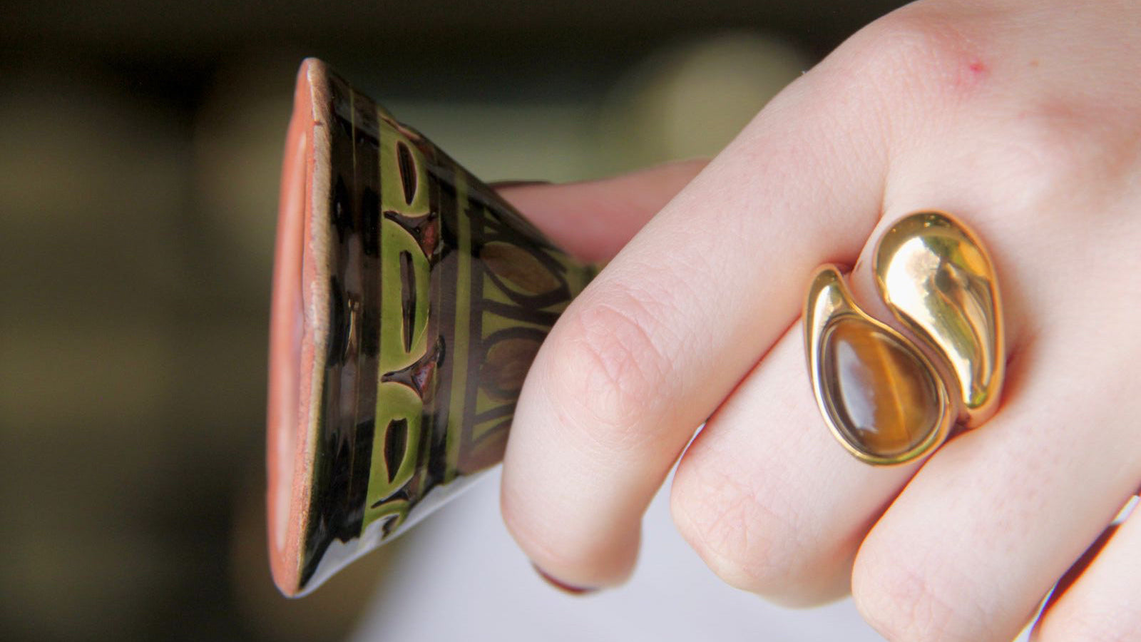 Gold ring on a hand holding a ceramic cup with a blurred background